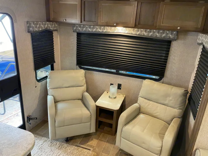 Inside an RV rental: inviting living space with two comfy light recliners, a side table with lamp, and wood cabinets.. Coleman Lantern 2019