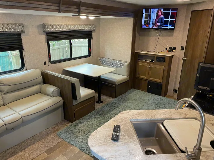 Cozy RV rental interior shows living space, dining booth, kitchen counter with sink, and wall-mounted TV.. Coleman Lantern 2019