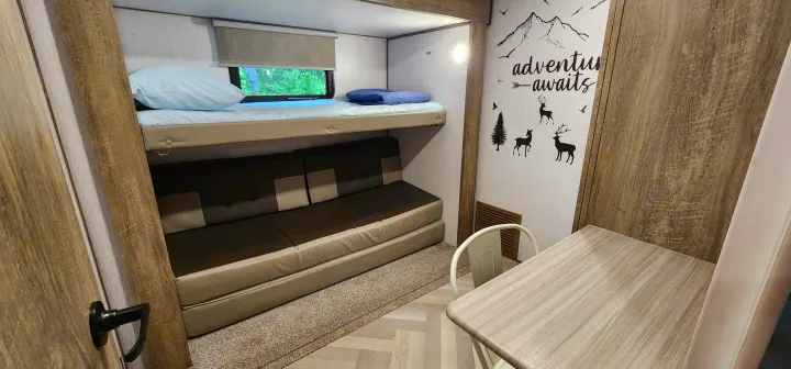 An RV rental interior showing bunk beds, a convertible sofa, and a dining table with "adventure awaits" wall art. Ready for your trip!. Forest River Hemisphere 2022
