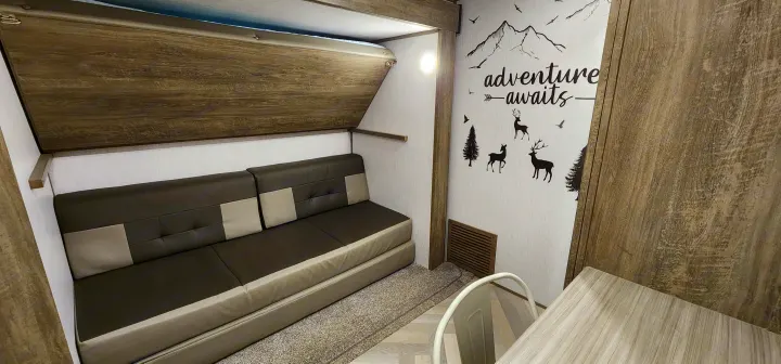This RV rental interior features a convertible sofa bed, an upper bunk, and an "adventure awaits" wall decal, perfect for compact travel.. Forest River Hemisphere 2022