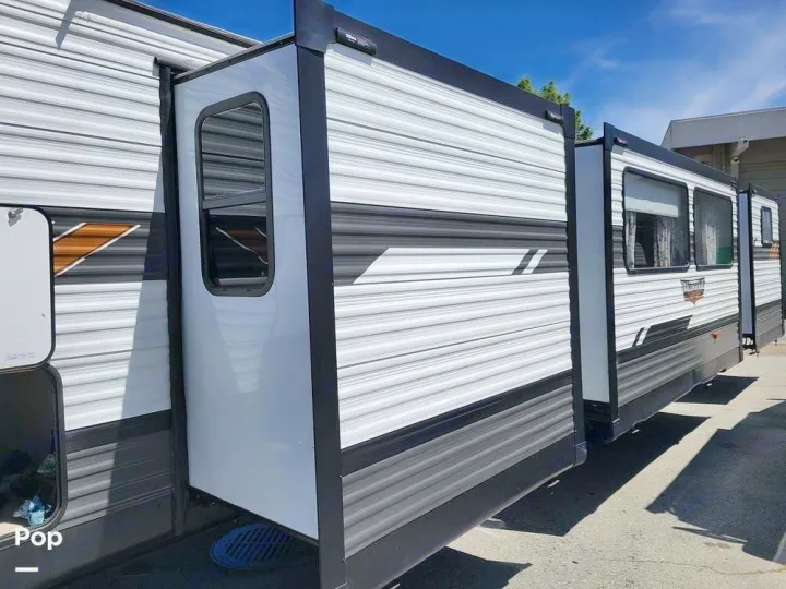 Side view of a white and grey RV rental with extended slide-outs, showcasing its spacious multi-section design.. Forest River Wildwood 2022