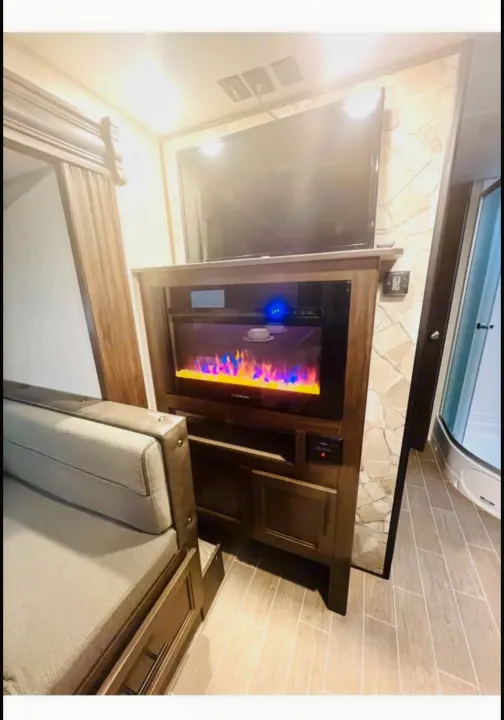 Cozy RV rental interior with a flat-screen TV above an electric fireplace, sofa, and a curved shower.. Forest River Cherokee Grey Wolf 2020