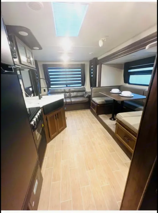 Modern RV rental interior: well-equipped kitchen, U-shaped dinette, and sofa. Bright, clean space with wood-look floor.. Forest River Cherokee Grey Wolf 2020