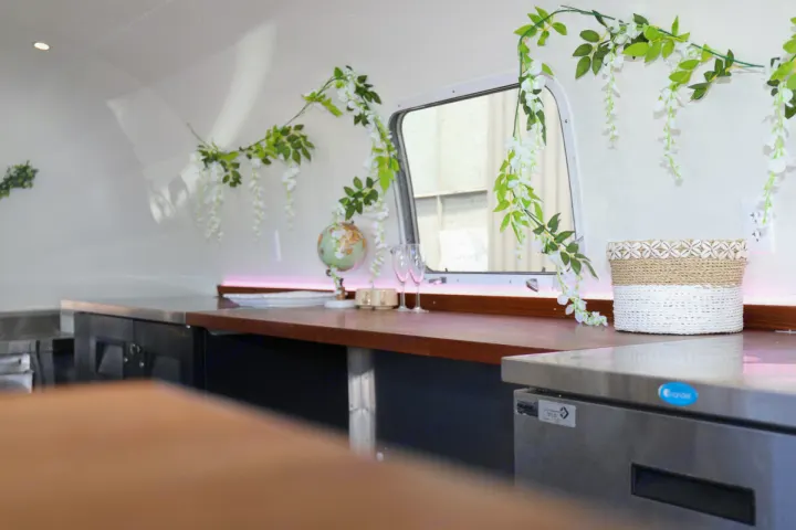 Interior of an rv rental mobile bar, adorned with elegant floral garlands, a wooden counter, and subtle pink lighting.. Airstream custom 1973