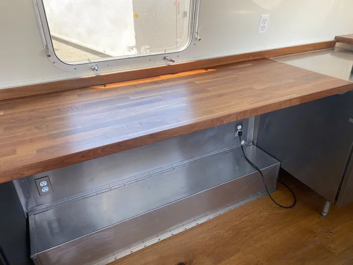 RV rental: Bright interior showing a long wooden countertop over stainless steel panels, with a large window.. Airstream custom 1973