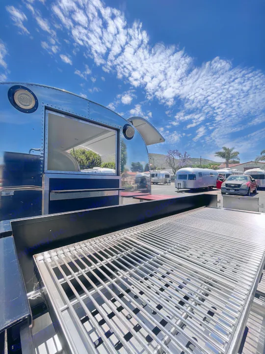 Large outdoor grill in front of a shiny Airstream food trailer, parked in an RV lot with other trailers, ideal for rv rental.. Airstream Custom 1957