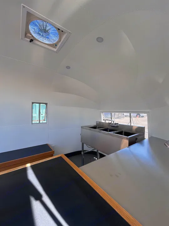 RV rental: Clean, mobile kitchen interior featuring commercial sinks, counters, and ceiling fan for food prep.. Airstream Custom 1957