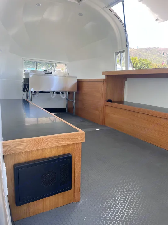 Spacious, clean RV rental interior featuring a stainless steel sink, wood counters, and textured floor, ready for customization.. Airstream Custom 1957