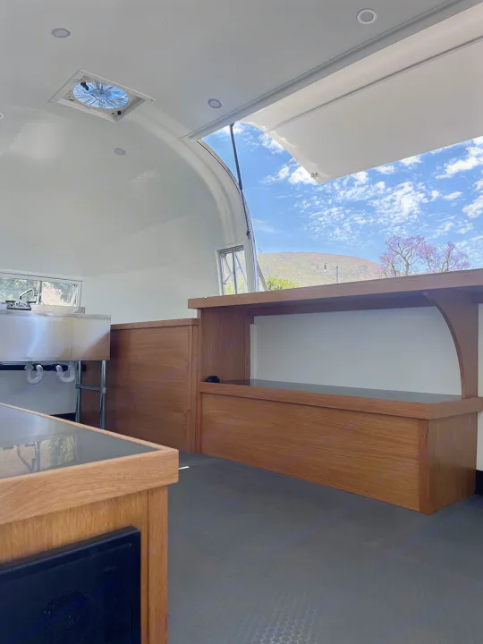 RV rental: Bright, clean mobile kitchen interior with custom wood cabinetry, stainless sink, and open service window.. Airstream Custom 1957