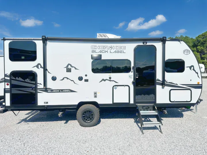 This white & black Cherokee Black Label travel trailer is an RV rental, ready for adventure. Steps are down on gravel.. Forest River Cherokee Wolf Pup 2025