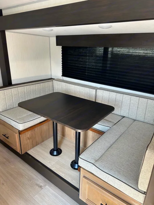 Spacious RV rental dinette with a dark table, light grey booth seating, and storage drawers. Perfect for travel adventures.. Forest River Cherokee Wolf Pup 2025