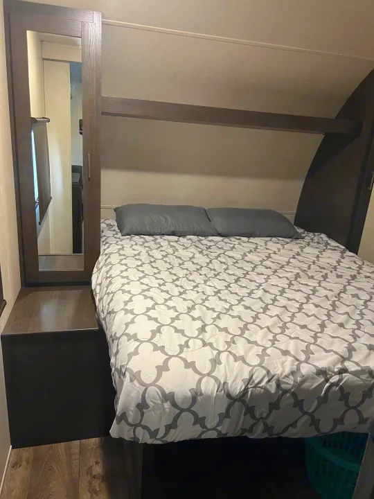 Cozy RV rental bedroom features a bed with a patterned comforter, mirrored wardrobe, and overhead storage.. Forest River Salem 2019