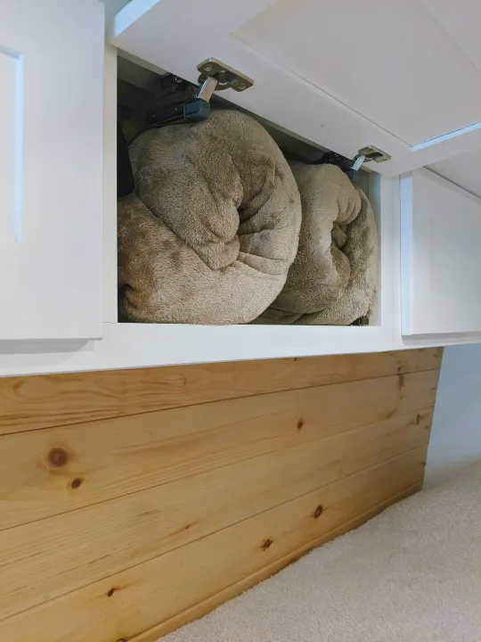 RV rental organized storage: Two soft, rolled blankets neatly inside an overhead white cabinet, above natural wood paneling.. Sprinter Mercedes 2018