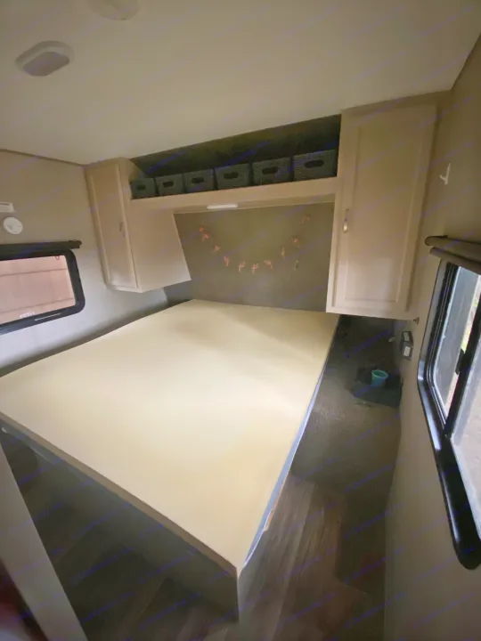 Clean RV rental bedroom with a bed platform, overhead storage bins, and side cabinets.. Keystone RV Summerland 2018