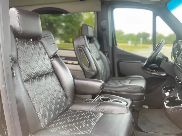 Comfortable RV rental interior: black leather captain's chairs with diamond stitching, armrests, steering wheel, and cupholders.. Mercedes Benz Sprinter 3500 2022