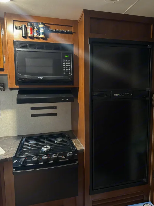 Compact RV rental kitchen featuring a microwave, gas stove, refrigerator, and spice holder for convenient cooking.. Jayco Jay Flight SLX Baja Edition 2017