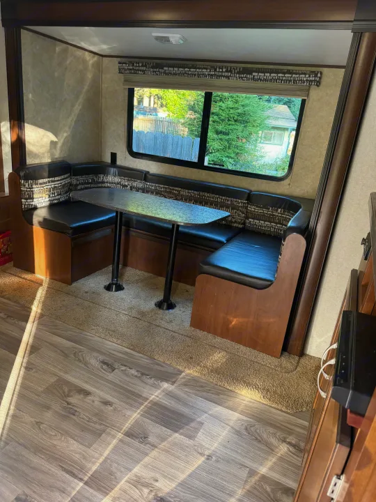 RV rental interior featuring a cozy dinette with U-shaped booth seating and a table, bathed in sunlight from the window.. Jayco Jay Flight SLX Baja Edition 2017