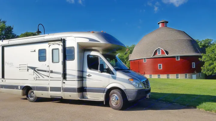Class C RV rental, a Coachmen Prism, parked next to a historic red round barn under a clear blue sky.. Coachmen Prism 2009