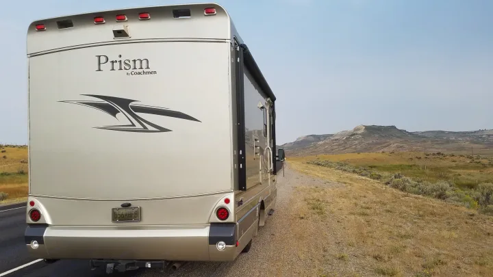 Rear view of a Coachmen Prism RV rental parked roadside in a dry, mountainous landscape under a clear sky.. Coachmen Prism 2009