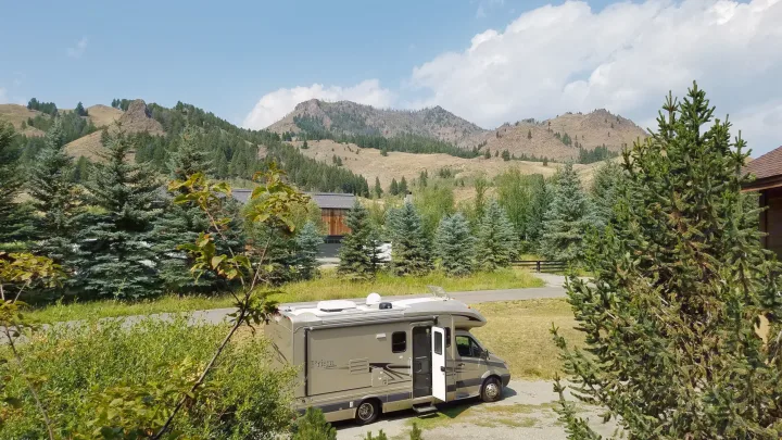 RV rental motorhome parked on gravel in a scenic mountain setting with evergreen trees and open door.. Coachmen Prism 2009