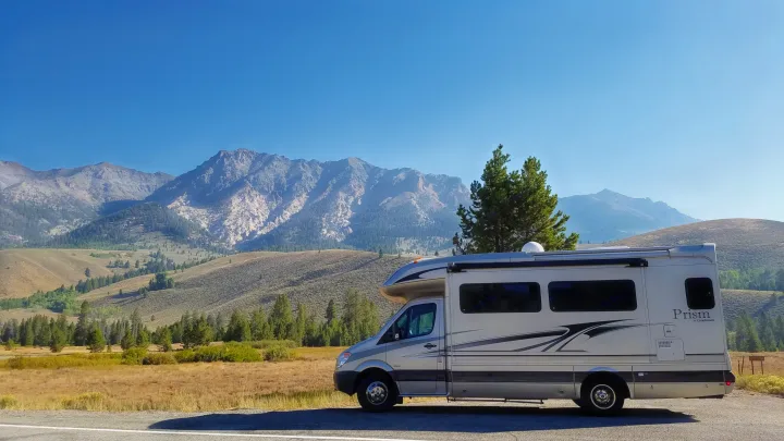 Silver RV rental parked roadside with stunning mountain views under a clear blue sky. Perfect for a scenic road trip!. Coachmen Prism 2009