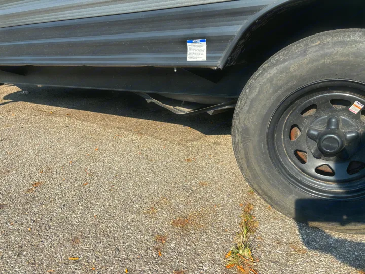 A close-up of an RV rental trailer's side and wheel on asphalt, featuring a safety notice about checking wheel lug nuts.. Forest River Wildwood 2021
