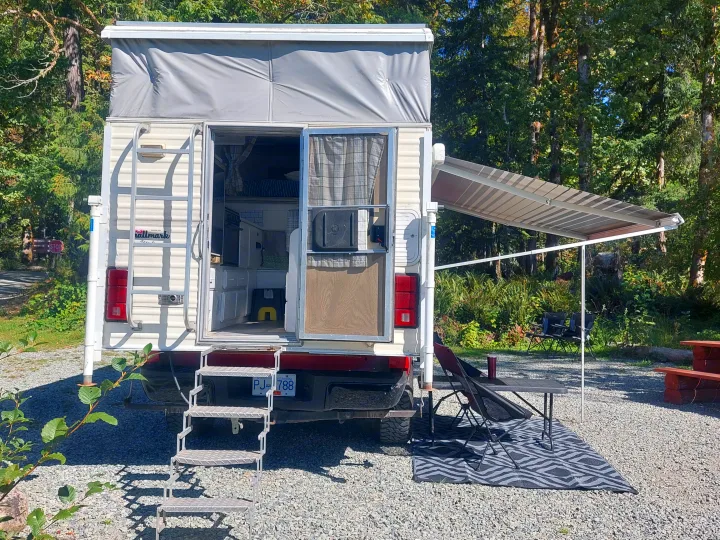 RV rental pop-up truck camper at a BC campsite. Awning, chairs, and table set up.. Ford F350 2015