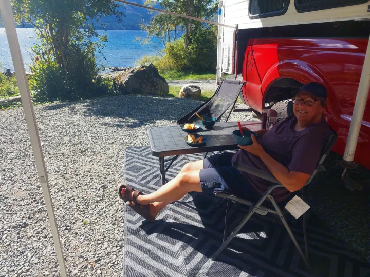 Relaxing at a beautiful lakefront RV rental campsite. A person enjoys snacks under the awning of their RV.. Ford F350 2015