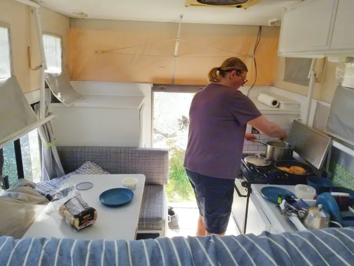 Inside a cozy RV rental, a person prepares a meal in the compact kitchen, with a dining booth nearby.. Ford F350 2015