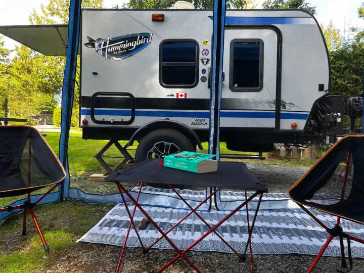 A cozy RV rental campsite with a Jayco Hummingbird, chairs, a table, and a book under an extended awning.. Jayco Hummingbird 2019