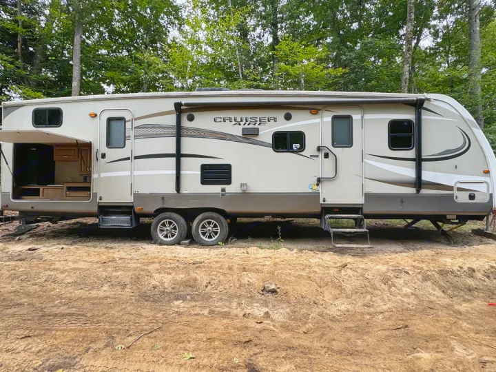 This RV rental, a Cruiser Aire travel trailer, is set up in a wooded campsite with an open outdoor kitchen.. Crossroads RV Cruiser Aire 2016