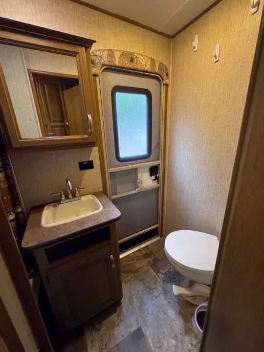 Compact RV rental bathroom: includes sink, mirror cabinet, toilet, and the RV's exterior door.. Crossroads RV Cruiser Aire 2016