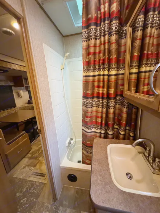 Compact rv rental bathroom featuring a tub/shower, vanity with sink, and Aztec-patterned curtain, opening to the living area.. Crossroads RV Cruiser Aire 2016