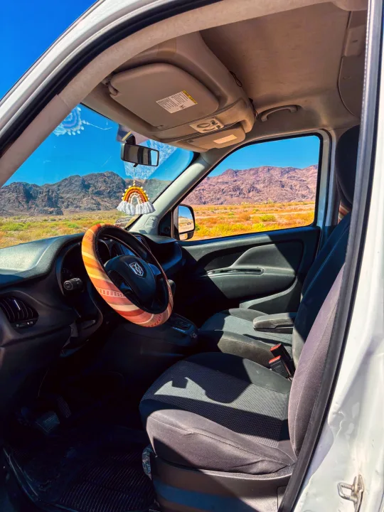 RV rental van interior showcases desert mountains and blue sky, with a cozy steering wheel cover, perfect for a scenic adventure.. Dodge Promaster City 2016