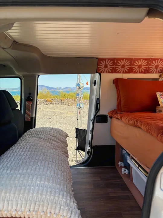 RV rental interior: cozy bed, wood floor, and stunning lake & mountain views. Ideal for a relaxing road trip van conversion.. Dodge Promaster City 2016