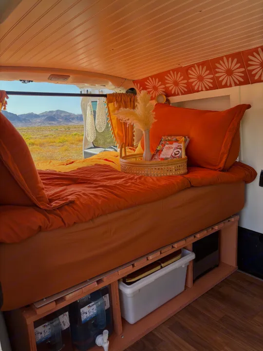 Cozy RV rental bedroom with orange bedding, mountain views, and smart under-bed storage for van life adventures.. Dodge Promaster City 2016