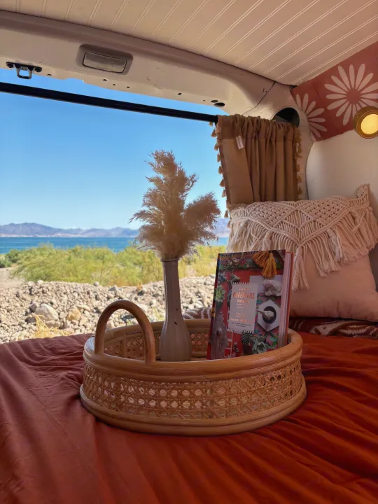 Cozy RV rental interior offers a serene lake view, perfect for van life adventures. Features a wicker tray with a book.. Dodge Promaster City 2016