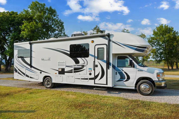 This white Entegra Odyssey RV rental, with black and blue graphics, is parked on a gravel path, ready for adventure.. Entegra Coach Odyssey 2020