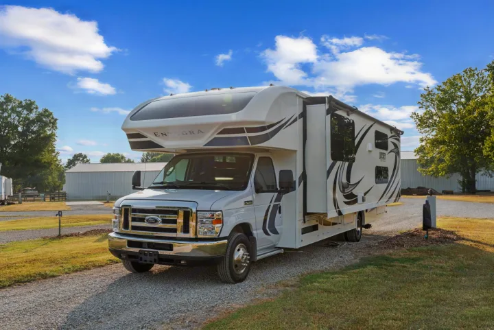White Entegra Odyssey Class C RV rental parked on a gravel driveway under a blue sky, ready for your next adventure.. Entegra Coach Odyssey 2020
