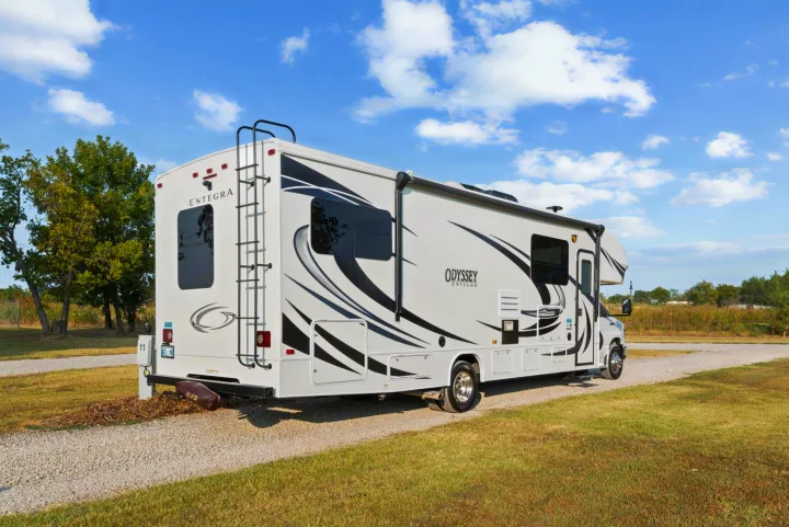 White Entegra Odyssey RV, perfect for an rv rental, parked on a gravel pad at a sunny campground.. Entegra Coach Odyssey 2020