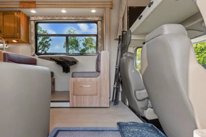 View inside an RV rental showing a dinette with a wall-mounted table, kitchen, and front cab with an overhead bed.. Entegra Coach Odyssey 2020