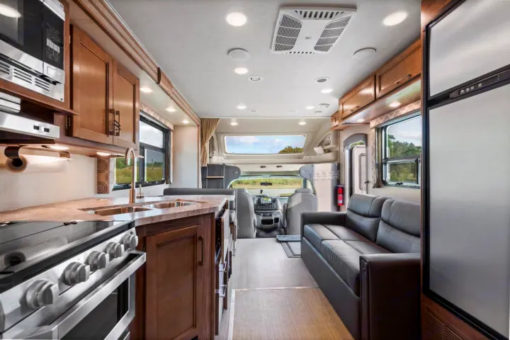 Explore this bright RV rental interior, showcasing a well-equipped kitchen, comfortable sofa, and front driving area.. Entegra Coach Odyssey 2020