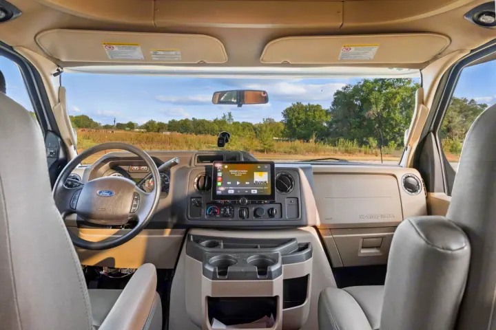 Spacious RV rental cockpit with a Ford dashboard, large infotainment screen playing music, and an open road view.. Entegra Coach Odyssey 2020