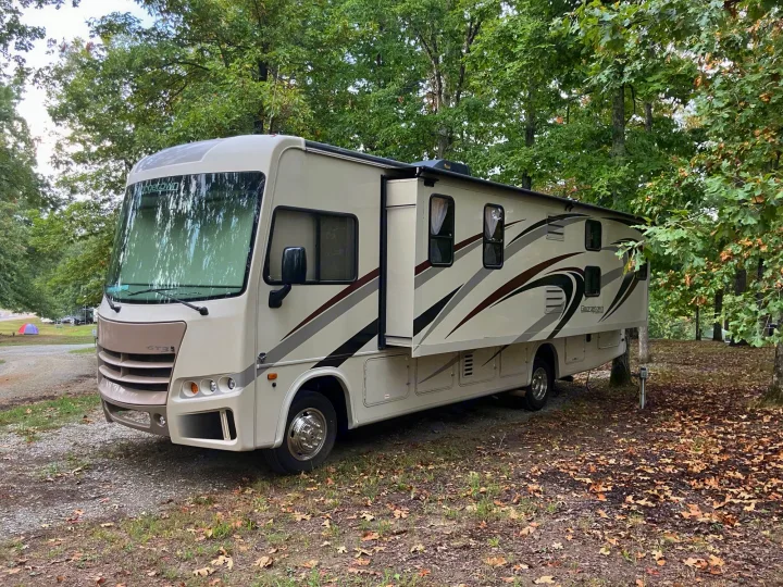 Spacious cream RV rental parked at a leafy campsite with a slide-out extended, surrounded by tall trees.. Georgetown GT3 2016
