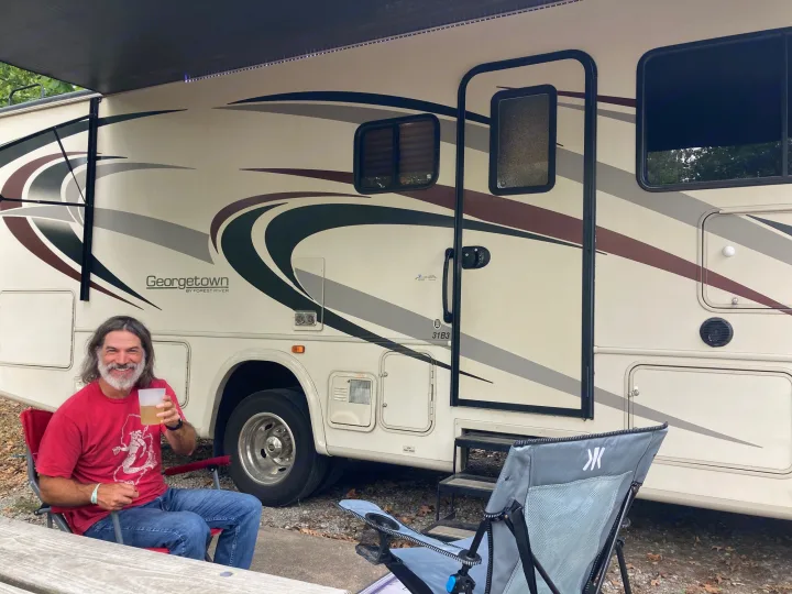 Man enjoys a drink by his Georgetown RV rental, parked at a peaceful campsite. Perfect for travel & leisure.. Georgetown GT3 2016