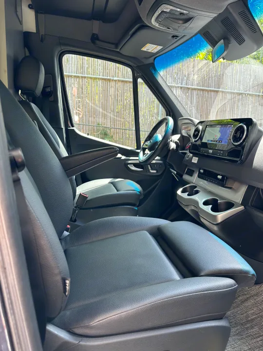 Interior view of an RV rental: front cabin with dark seats, modern dashboard, and navigation screen.. Thor Sanctuary 2023