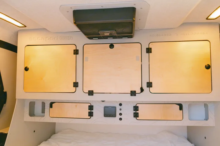 Modern Escapod rv rental interior with wooden cabinets, ceiling fan, and controls above a bed.. Escapod Topo 2 Voyager 2024