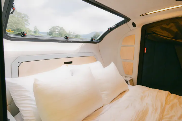 An RV rental's cozy interior features a comfortable bed, large window with a scenic view, and warm lighting.. Escapod Topo 2 Voyager 2024