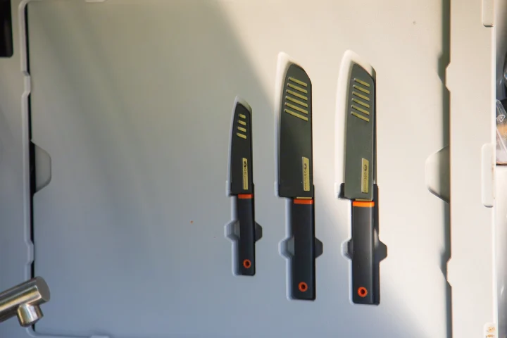 Organized GSI Outdoors knife set in an RV rental. Three black knives with orange handles and striped sheaths, perfect for cooking on the go.. Escapod Topo 2 Voyager 2024