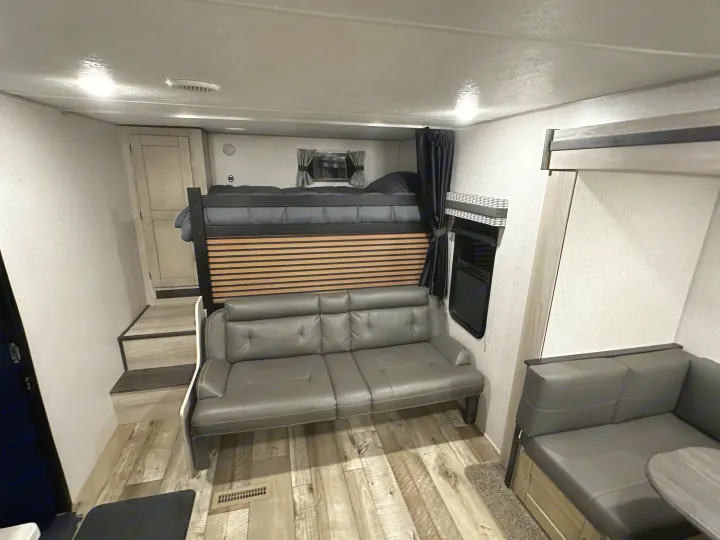 Spacious RV rental interior showing a bunk bed over a sofa, a dinette booth, and modern wood-look flooring.. Connect SE 2022